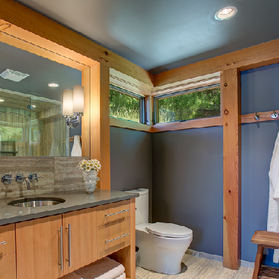 Next to the house entry, the spa-like bathroom shows off with its elegant sink, toilet, cabinet storage and a modern shower reflected in the mirror. (Fine Homebuilding)
